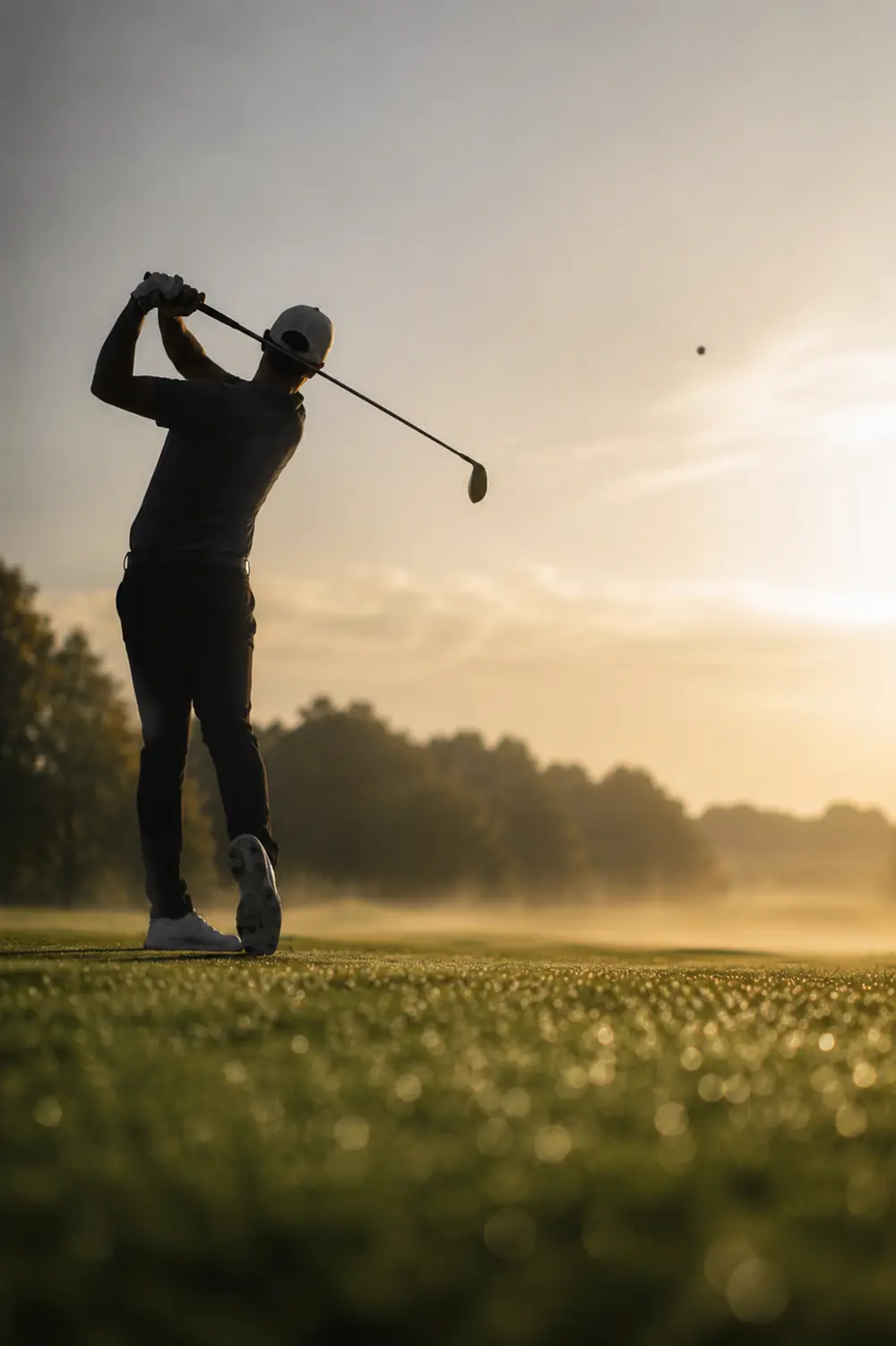 Golfer beim Abschlag im Abendlicht